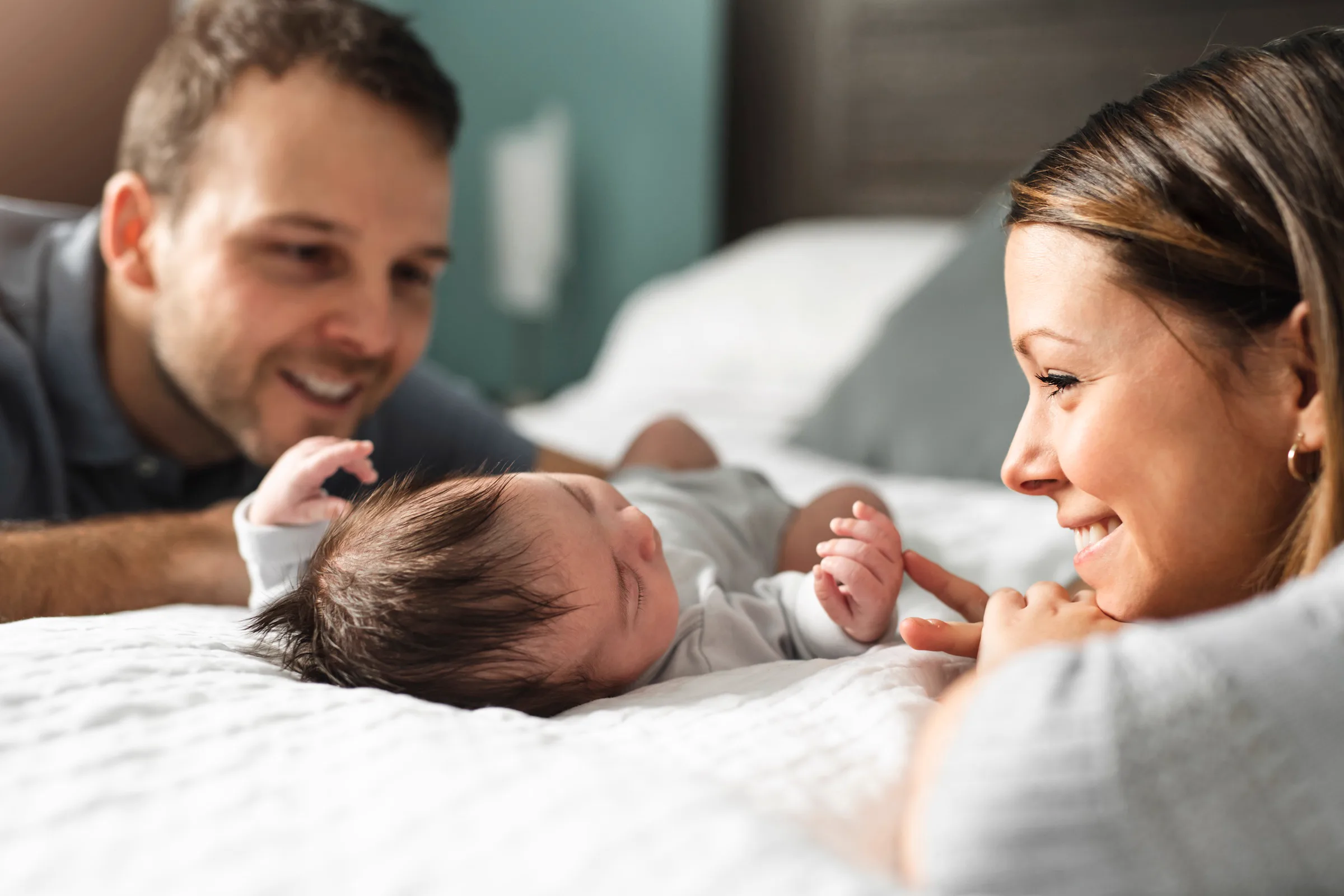 Eltern liegen mit ihrem lachenden Baby auf dem Bett