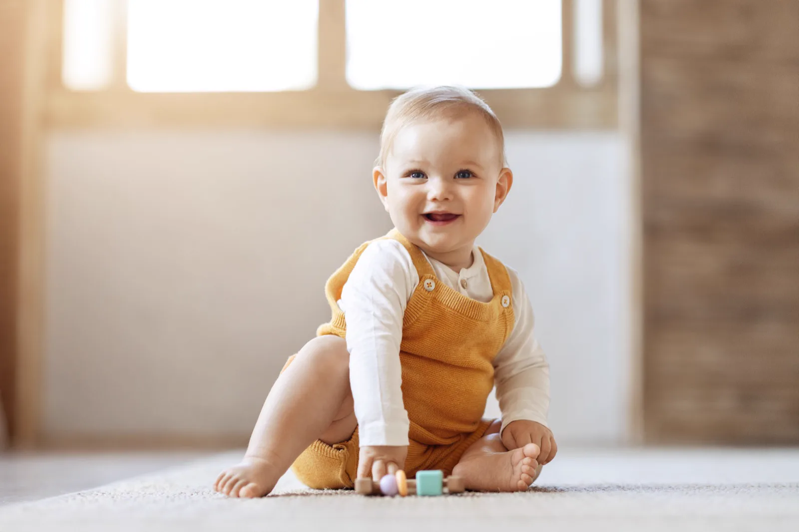 Baby beim Spielen Lächelndes Baby sitzt mit Holzspielzeug auf dem Boden